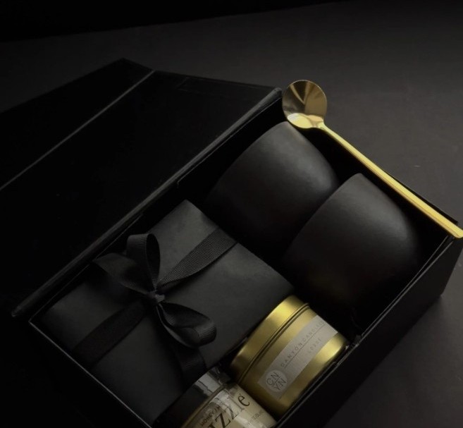 Black ceramic cups with a gold spoon and candle in a gift box